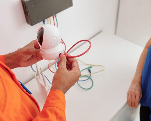 Close-up of unrecognizable man holding wired camera and installing at home under control of house owner